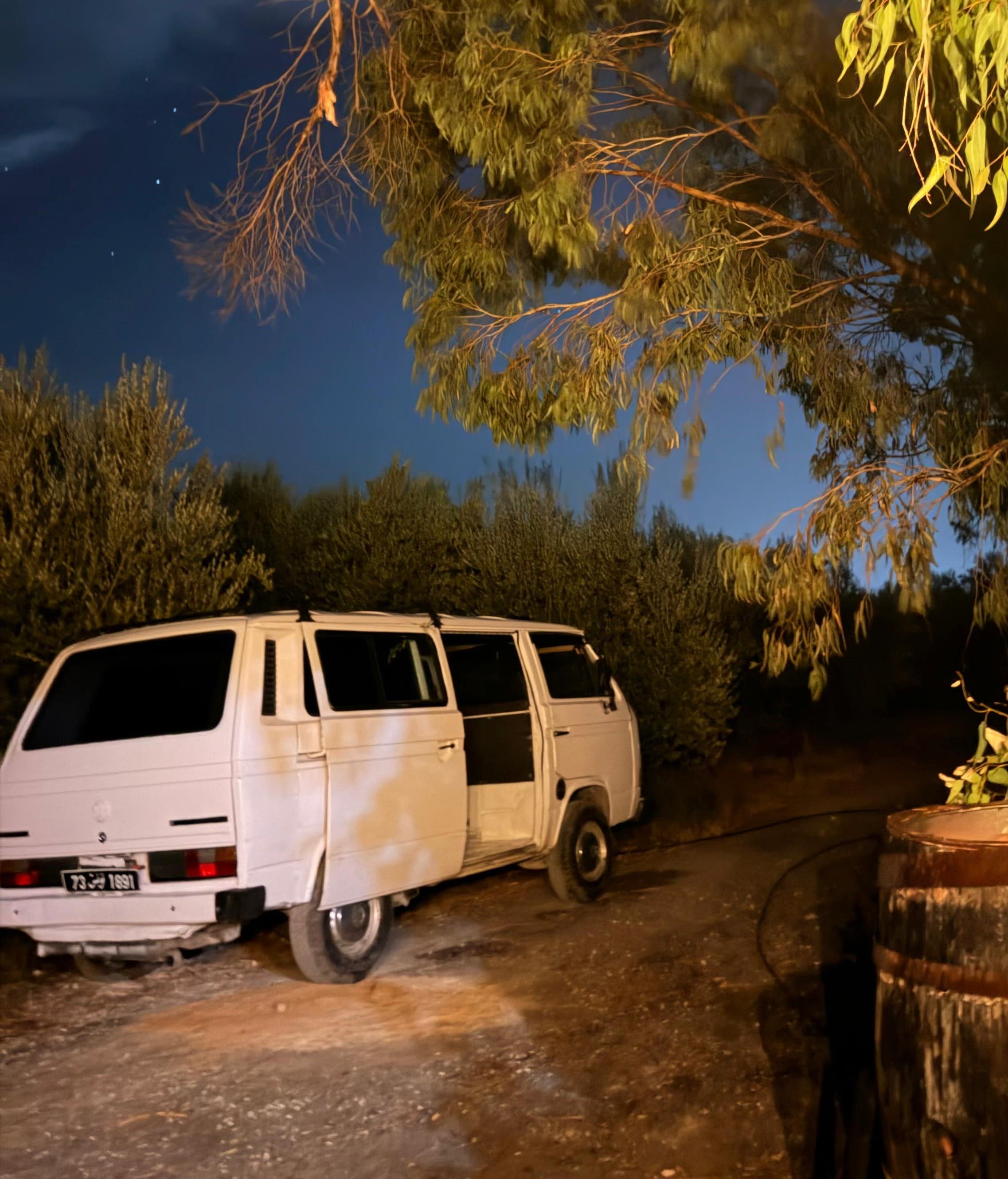 Un van blanc stationné sous les arbres à Farm El Baya la nuit